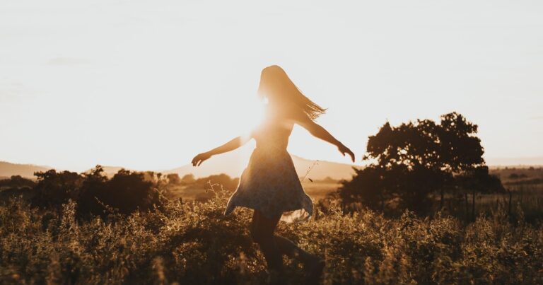 A girl spins in a field wearing a summer dress as the sun is setting.